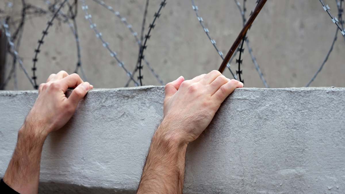 Uciekł z więzienia i opublikował to na TikToku: ręce na murze z tyłu drut kolczasty