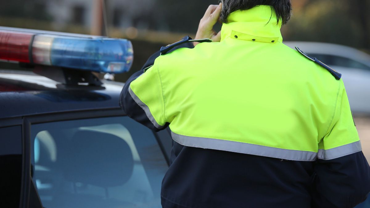 Maraton fotoradarów sierpień 2025 . Policjant w kurtce przy radiowozie podczas rozmowy przez telefon